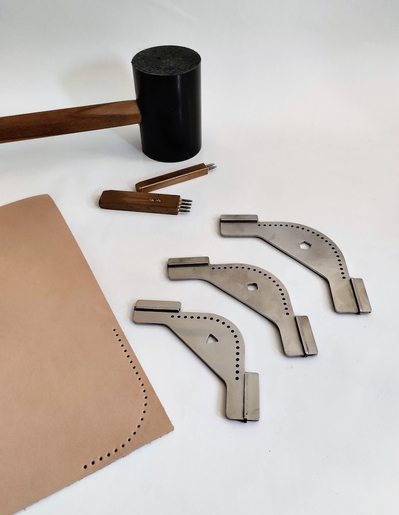 Peut inclure: Des outils de maroquinerie sont dispos&eacute;s sur une surface blanche. Un maillet noir avec un manche en bois est &agrave; c&ocirc;t&eacute; d'outils en m&eacute;tal, notamment des poin&ccedil;ons et des guides de bord incurv&eacute;s. Une pi&egrave;ce de cuir beige avec des trous pr&eacute;-perc&eacute;s est &eacute;galement pr&eacute;sente.