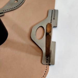 Peut inclure: Outils de maroquinerie et un morceau de cuir brun clair. Les outils sont en m&eacute;tal argent&eacute; et ont diverses formes avec des trous pour la couture. Le cuir a un bord incurv&eacute; avec des trous espac&eacute;s uniform&eacute;ment.