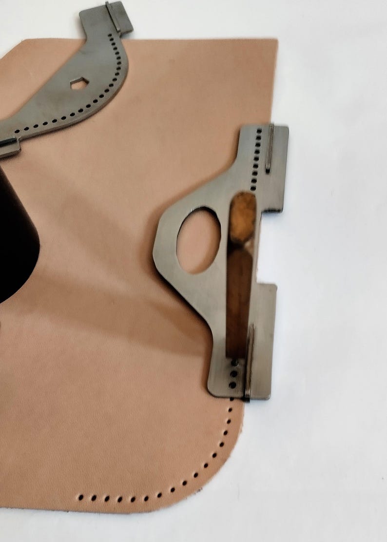 Peut inclure: Outils de maroquinerie et un morceau de cuir brun clair. Les outils sont en m&eacute;tal argent&eacute; et ont diverses formes avec des trous pour la couture. Le cuir a un bord incurv&eacute; avec des trous espac&eacute;s uniform&eacute;ment.