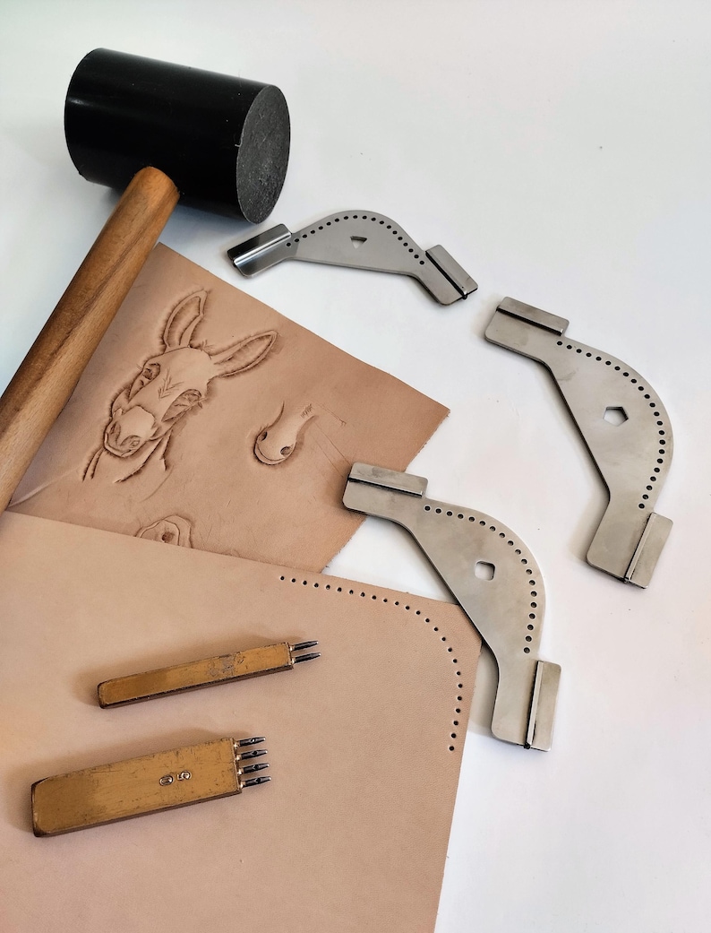 Peut inclure: Ensemble d'outils de travail du cuir, dont un maillet noir, des tampons m&eacute;talliques et des al&egrave;nes &agrave; coudre. Une pi&egrave;ce de cuir beige pr&eacute;sente un motif d'&acirc;ne en relief et des marques de points perfor&eacute;s.