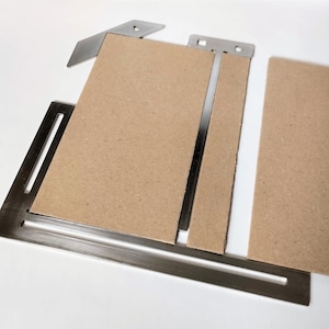 May include: A set of metal tools with brown cardboard. The tools are designed for precise cutting or measuring, featuring a rectangular base and angled components. The cardboard is a light brown colour.