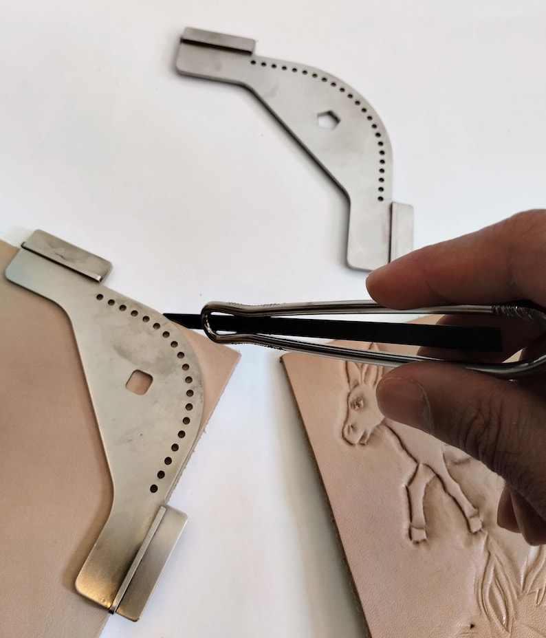 Peut inclure: Outils de travail du cuir en acier inoxydable. L'image montre un rainureur &agrave; coudre en m&eacute;tal et deux gabarits m&eacute;talliques avec des trous espac&eacute;s. Un morceau de cuir avec un motif d'&acirc;ne est &eacute;galement visible. Ces outils sont utilis&eacute;s pour le travail du cuir.