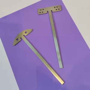 Puede incluir: Dos herramientas de metal con mangos y cabezas de diferentes formas. Las herramientas están sobre una superficie morada.