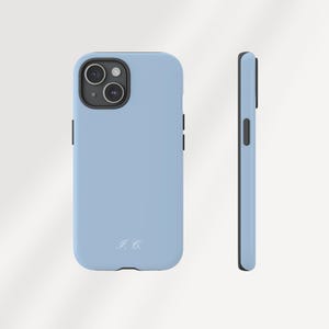 May include: A light blue phone case with a black border. The case has a camera cutout and a small, white inscription at the bottom. The phone case is shown from the front and side.