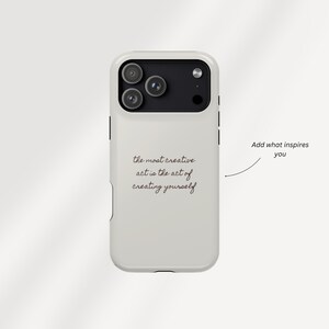 May include: A white phone case with a black camera module. The case features the quote, "the most creative act is the act of creating yourself" in black script. The phrase "Add what inspires you" is also present.