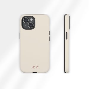 May include: A cream-colored phone case with a black border. The case features a dual-lens camera cutout and the initials "M. C." in a burgundy script. The side view shows the case's slim profile.