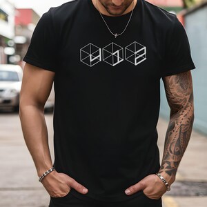 Peut inclure: T-shirt noir avec un motif géométrique blanc de trois cubes connectés. Le t-shirt est à manches courtes et a un col rond. La personne portant le t-shirt porte un collier et un bracelet argentés.