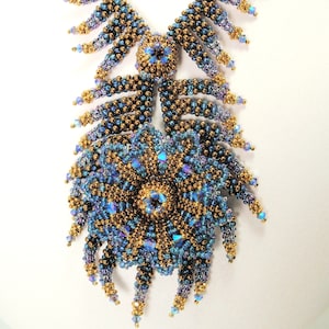 May include: A beaded necklace featuring a large, elaborate flower design in shades of blue and gold. The necklace is crafted from small, round beads and has a cascading fringe.