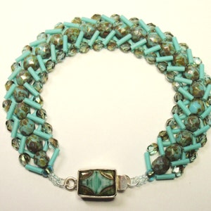 May include: A turquoise and brown beaded bracelet with a silver clasp. The bracelet is made with a variety of beads, including small round beads, larger oval beads, and small cylinder beads.