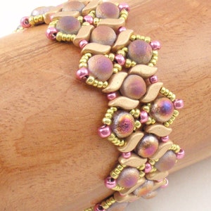 Może przedstawiać: Bransoletka z koralików różowych i złotych w geometryczny wzór. Bransoletka wykonana jest z małych, okrągłych koralików i większych, płaskich, tęczowych koralików.