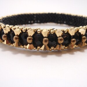 May include: A black and gold beaded bracelet with a geometric design. The bracelet is made with small, round beads and larger, faceted beads.