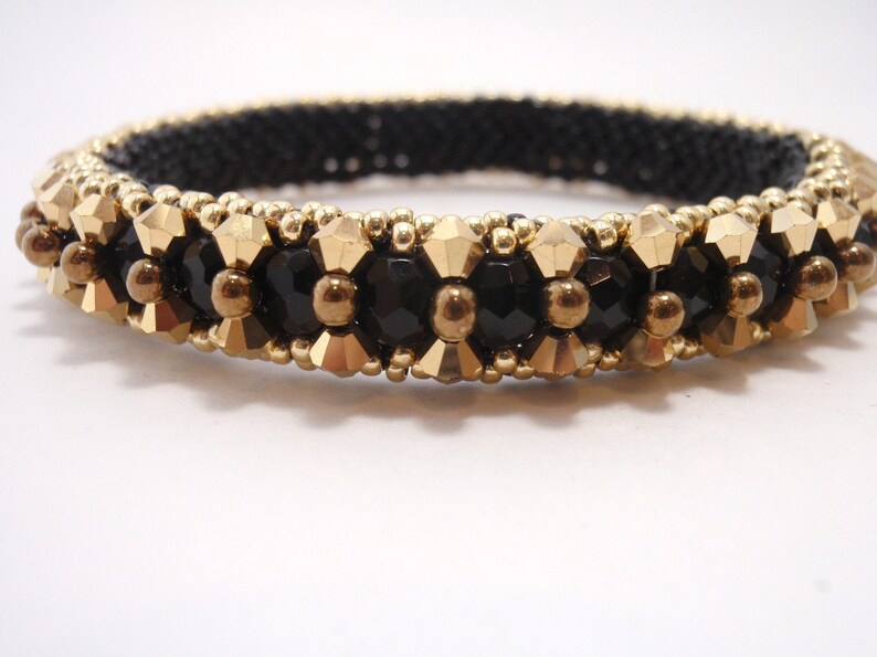 May include: A black and gold beaded bracelet with a geometric design. The bracelet is made with small, round beads and larger, faceted beads.