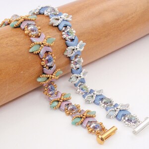 May include: Two beaded bracelets with a geometric pattern. One bracelet is silver and blue with iridescent beads, the other is gold and pink with iridescent beads.