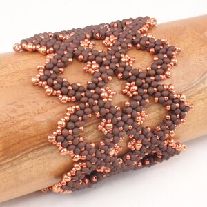 May include: A brown and copper beaded bracelet with a geometric design. The bracelet is made of small, round beads that are woven together in a intricate pattern.