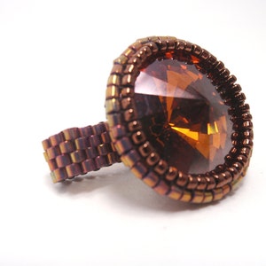 May include: A ring with a large, faceted, amber-colored gemstone set in a bezel of copper-colored beads.