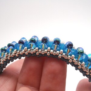 May include: A beaded bracelet with a blue and silver color scheme. The bracelet is made with small, round beads and has a textured, woven look.