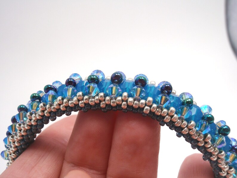 May include: A beaded bracelet with a blue and silver color scheme. The bracelet is made with small, round beads and has a textured, woven look.