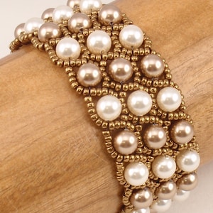 Può includere: Un braccialetto di perline dorate e bianche con un motivo intrecciato. Il braccialetto è realizzato con piccole perline dorate e perle più grandi bianche e dorate.