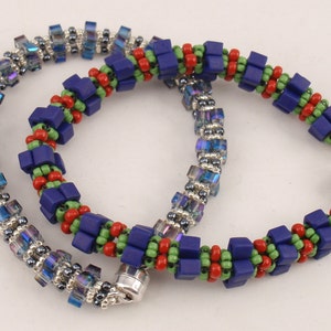 Könnte beinhalten: Zwei Perlenarmbänder, eines mit blauen, grünen und roten quadratischen Perlen und das andere mit schillernden blauen und silbernen Perlen.