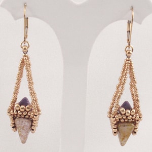 Könnte beinhalten: Goldfarbene Ohrhänger mit geometrischem Design. Die Ohrringe haben einen dreieckigen Anhänger mit einem violetten und braunen Stein in der Mitte.