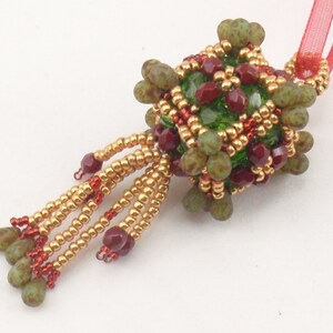 May include: A green and red beaded ornament with a gold tassel. The ornament is shaped like a sphere and has a red ribbon attached to it.