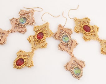 May include: A pair of gold and rose gold earrings with red and green glass beads. The earrings are made of intricate designs and have a dangling style.
