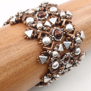 Könnte beinhalten: Ein silbernes und braunes Perlenarmband mit geometrischem Muster. Das Armband besteht aus kleinen, runden Perlen und dreieckigen Perlen.