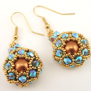 May include: A pair of gold earrings with a round, iridescent blue and gold bead design. Each bead is surrounded by smaller gold beads and a larger, copper-colored bead in the center.