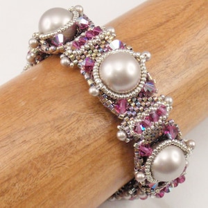 Puede incluir: Un brazalete de cuentas con tres perlas grandes de color blanco roto y cuentas rosas y plateadas.