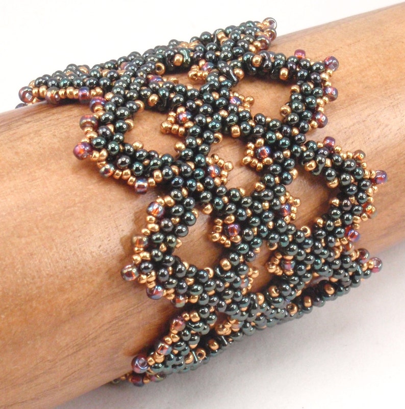 May include: A dark green and copper beaded bracelet with a delicate, intricate design. The bracelet is made with small, round beads that are woven together in a complex pattern.