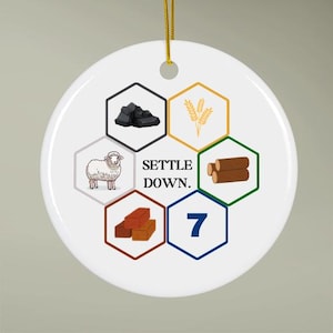 May include: White ceramic ornament with a hexagonal design. Each hexagon features a different image: a sheep, a pile of coal, a stack of logs, a brick, a number 7, and a wheat stalk. The text "Settle Down." is printed in the center of the ornament.