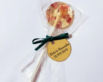 May include: A clear lollipop with embedded red and white pieces, wrapped in cellophane. The lollipop is attached to a white stick and tied with a dark green ribbon and a gold tag that reads "Date to Remember 12/09/2019".