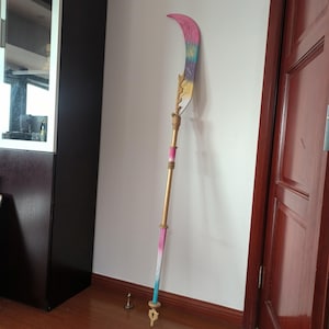 Puede incluir: Un arma de asta decorativa con una hoja curva. La hoja presenta un degradado de rosa, amarillo y azul. La pértiga es dorada con detalles en rosa y azul. Una pequeña base decorativa está en el suelo.