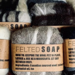 May include: A selection of felted soap bars, each with a brown paper label. The labels read "FELTED SOAP" and include instructions. The soap is made from a mix of grey, white, and black wool. The text on the label says "How to: Keeping the wool felt in place, lather & use as a washcloth. Let dry between uses."