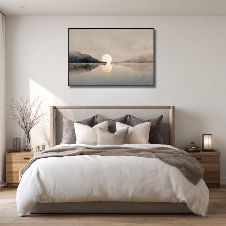 Könnte beinhalten: Ein gerahmter Kunstdruck, der eine ruhige Seeansicht mit einer großen, hellen Sonne zeigt, die sich im Wasser spiegelt. Das Kunstwerk ist über einem Bett mit neutralfarbener Bettwäsche, Kissen und einem hölzernen Kopfteil angebracht. Der Raum ist minimalistisch eingerichtet.