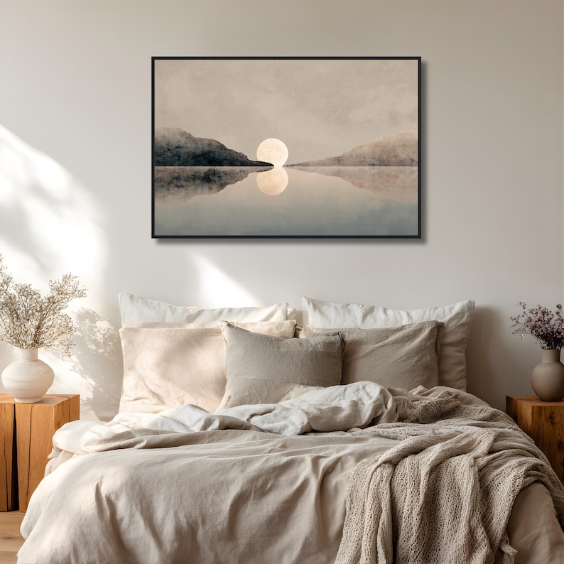 May include: A rectangular wall art print in a thin black frame featuring a landscape painting of a pale moon rising between two dark, silhouetted mountain ranges above a calm, reflective body of water in muted beige, gray, and blue tones.