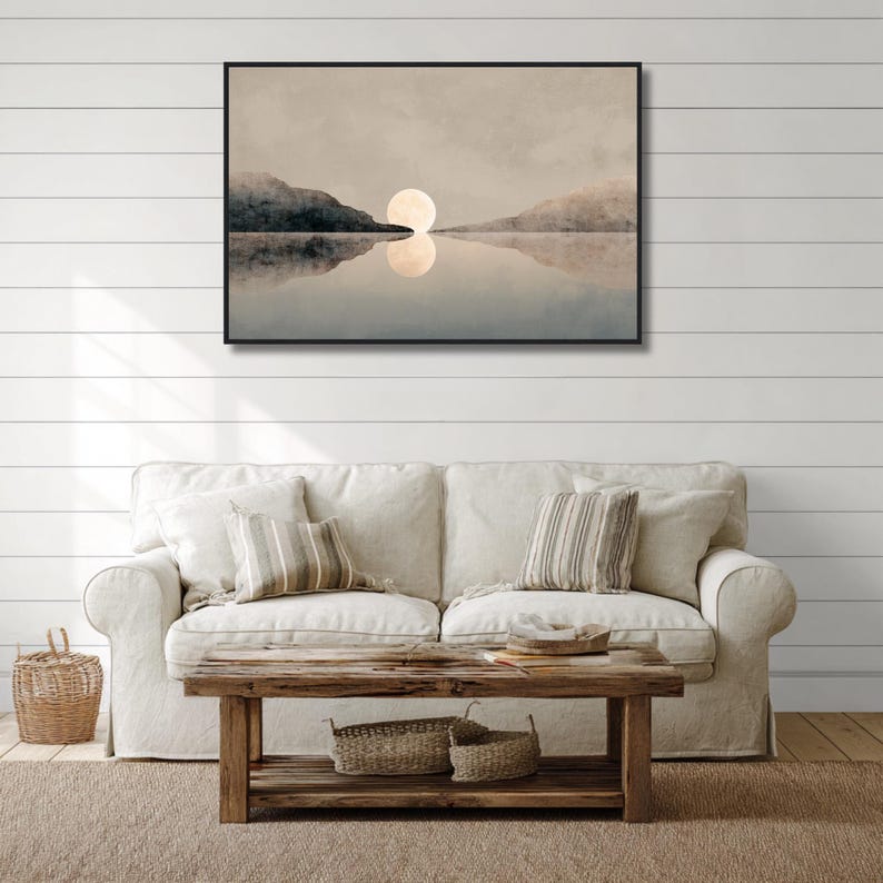 May include: A rectangular wall art print in a black frame featuring a landscape painting of a large, pale moon centered between two dark, silhouetted mountain ranges, with the moon and mountains reflected in the calm, still water below.