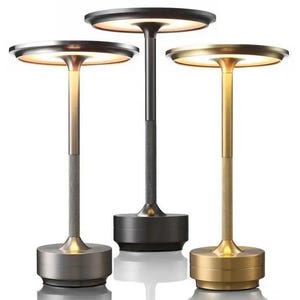 May include: Three modern table lamps in silver, black, and gold. Each lamp has a round, illuminated top, a textured stem, and a circular base. The lamps are designed for ambient lighting and decorative purposes.