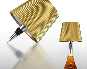 May include: A gold bottle stopper shaped like a lampshade. The stopper is shown on a bottle of liquor.