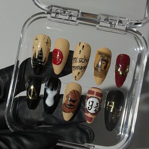Puede incluir: Un juego de diez uñas postizas en forma de almendra en un estuche de plástico transparente. Los diseños incluyen un castillo negro, un sello de cera rojo, el texto 'mischief managed', un cartel de 'Harry Potter', un símbolo dorado y 9 3/4.