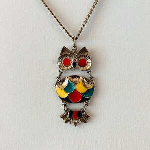 May include: A gold chain necklace with an owl pendant. The owl is made of metal and has red, yellow, green, and black enamel accents.