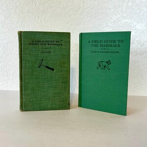 May include: Two vintage green field guide books. The book on the left is titled "A Field Guide to Rocks and Minerals" by Pough and features a small illustration of a rock hammer. The book on the right is titled "A Field Guide to the Mammals" by Burt & Grossenheider and features a small illustration of a lynx.