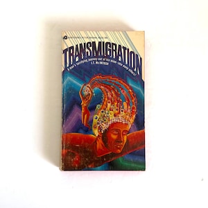 May include: A vintage paperback book titled Transmigration by J.T. McIntosh. The cover features a surreal illustration of a face with a colourful, swirling energy plume rising from the head, containing multiple smaller figures and abstract shapes.