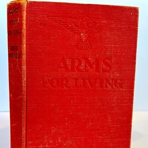 May include: A red hardback book with the title "Arms for Living" embossed on the front cover. The book features a stylised eagle design above the title.