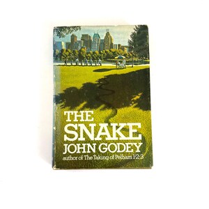 May include: A vintage paperback book titled "The Snake" by John Godey. The cover shows a green and yellow illustration of a park scene with a city skyline. The author's previous work, "The Taking of Pelham 1-2-3," is also listed on the cover.