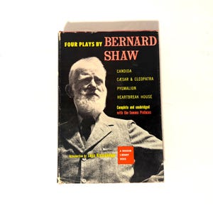 Könnte beinhalten: Ein Vintage-Buchcover für "Four Plays by Bernard Shaw". Das Cover hat einen schwarzen Hintergrund mit dem Namen des Autors in Rot und einem Porträt von Bernard Shaw. Das Buch enthält "Candida", "Caesar & Cleopatra", "Pygmalion" und "Heartbreak House".