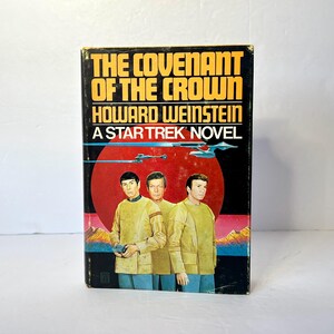 Puede incluir: Una portada de libro de bolsillo vintage para "The Covenant of the Crown", una novela de Star Trek de Howard Weinstein. La portada presenta un planeta rojo con tres hombres con uniformes amarillos de pie frente a él. El título del libro está en texto amarillo y negro.