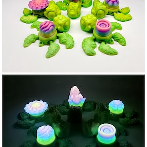 Könnte beinhalten: Eine Sammlung skurriler, pflanzenartiger Skulpturen in Grün-, Rosa- und Lilatönen. Das obere Bild zeigt die Skulpturen bei Tageslicht, während das untere Bild sie mit einem sanften, leuchtenden Licht zeigt.