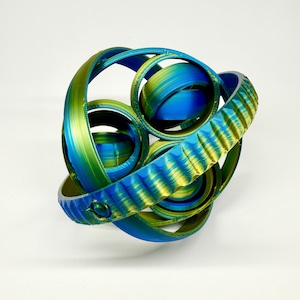 May include: A 3D-printed abstract sculpture with a complex, interwoven design. The piece features curved bands and circular elements in shades of blue, green, and yellow. The sculpture has a textured surface and is set against a white background.