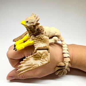 Puede incluir: Un juguete de grifo articulado y detallado con un cuerpo beige, alas marrones y garras amarillas. El grifo tiene un pico amarillo y está posado con las alas extendidas. El juguete es de plástico y tiene una cola segmentada.